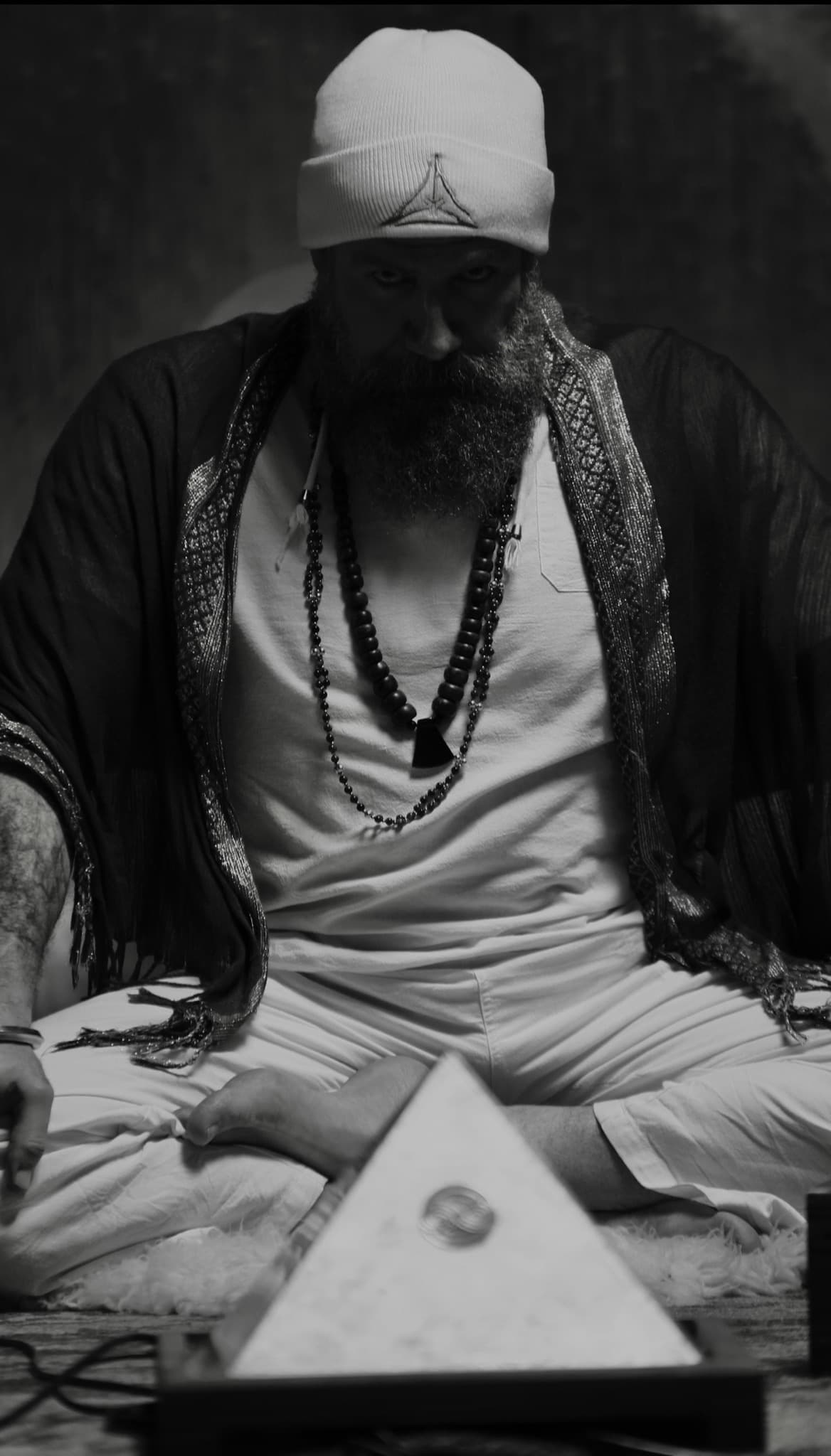 Mikal Vega seated in meditation before an illuminated pyramid.