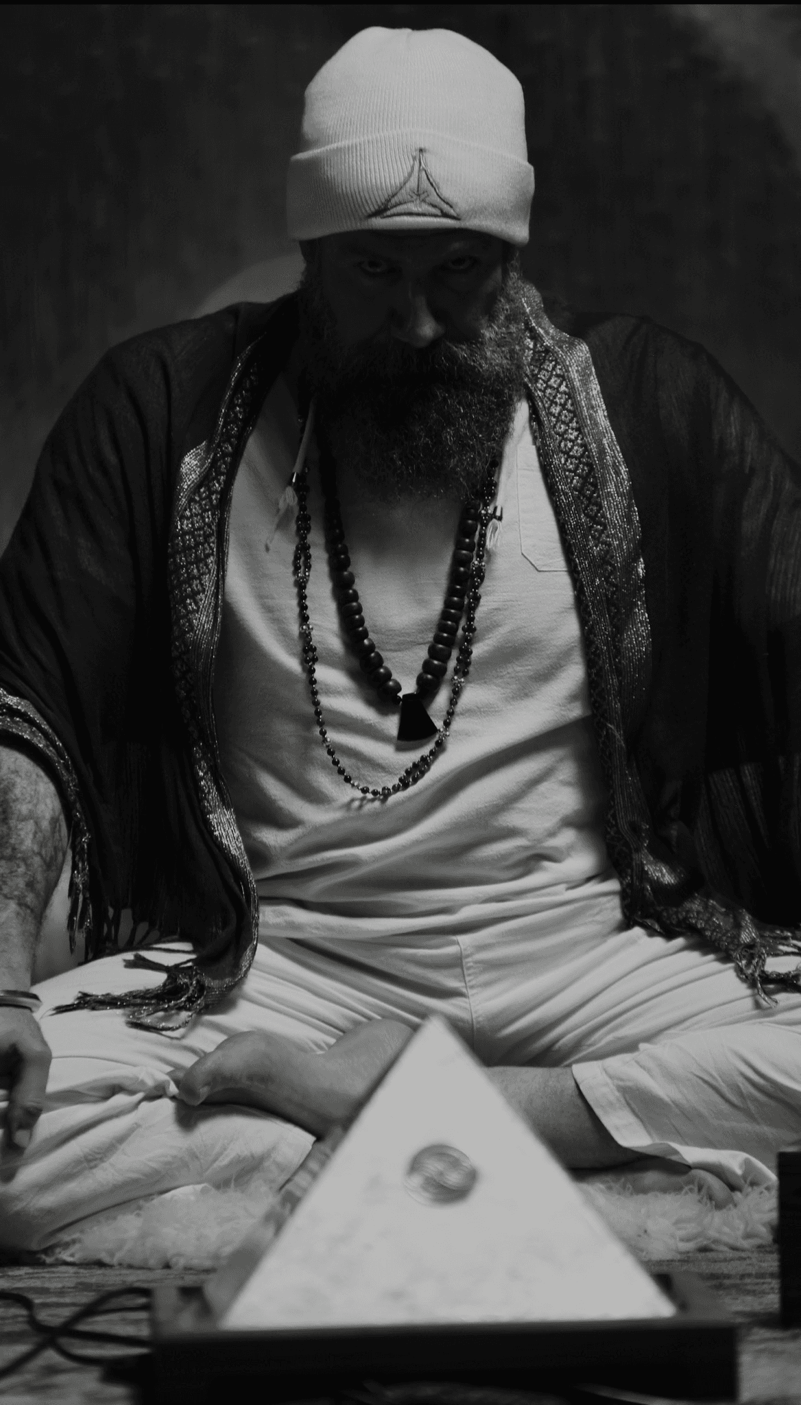 Mikal Vega seated in meditation before an illuminated pyramid.